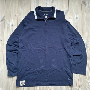 Marinblå half zip tröja från Ralph Lauren - Snygg marinblå långärmad tröja från Ralph Lauren med half zip och ståkrage med vita detaljer. Tröjan har broderad logga på bröstet och en cool patch längst ner. Perfekt för dig som gillar klassisk stil med sportig touch.