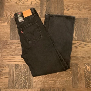 Levi's svarta jeans straight fit - Riktigt feta klassiska svarta Levi's jeans med klassisk straight fit och hög midja. Jeansen har fem fickor, knappgylf och den ikoniska läderpatchen bak i midjan. Tillverkade i slitstarkt bomullsjeansmaterial med en mörk ton och diskreta sömmar. W28 L29. Jeansen är helt nya och oanvända, med alla lappar kvar på. Vid frågor och funderingar, fråga på! 