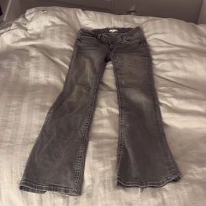 Grå bootcut jeans från Gina Tricot - Snygga grå jeans från Gina Tricot i storlek 164 med bootcut-ben och coola vita kontrastsömmar på bakfickan. Klassisk femficksmodell och mjukt jeanstyg som sitter skönt. Perfekt för dig som gillar en avslappnad och trendig look.