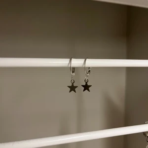 Silverörhängen med stjärnhänge - Snygga örhängen i silverfärg med små stjärnor som hänger ner från runda hoops. Perfekt för dig som gillar minimalistisk stil med en liten twist. Stjärnorna ger en cool och lekfull vibe till din look. Rostfritt stål och handgjort 