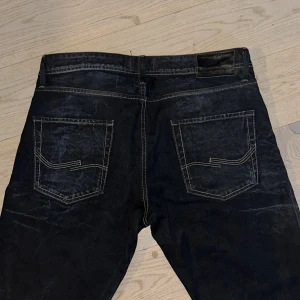 Jack&Jones VINTAGE CLOTH CO. mörkblå jeans med kontrastsömmar - Snygga Jack&Jones VINTAGE CLOTH CO.   jeans i mörkblå tvätt med klassiska kontrastsömmar och knäppning med knappar. Baktill finns två fickor med unik sömdesign och läderpatch i midjan. Perfekta för dig som gillar tidlös denimstil. Men snygga detaljer. Har hittat ett par liknande på nätet. Och dessa är en modell som ej tillverkats på länge. Storleks lappen är borta men jag har måttat och fått hjälp med att prova och dem är w33-34 och L34 