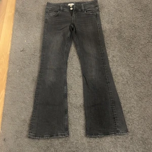 Svarta bootcut jeans Gina Tricot 146 - Snygga svarta jeans från Gina Tricot i storlek 146. Modellen har bootcut-ben, klassiska fem fickor och dubbla knappar fram. Jeansen har en mörk tvätt och är tillverkade i mjukt denim-material. Perfekt för dig som gillar retrovibbar och bekväm passform.