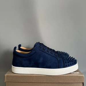 Mörkblå sneakers med nitar - Snygga mörkblå sneakers med platt vit sula och rund tå. Ovandelen är i mocka och har coola ton-i-ton nitar framtill som ger en edgy vibe. Skorna har snörning och en låg profil, perfekt för dig som vill sticka ut med din stil.