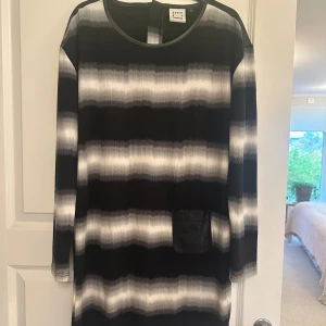 Randig klänning Karen by Simonsen - Snygg kort klänning med svart och grått randigt mönster från Karen by Simonsen. Långärmad modell med coola skinn detaljer upptill och på fickan. Dragkedja i ryggen ger en edgy touch. Perfekt för dig som gillar en modern och stilren look.
