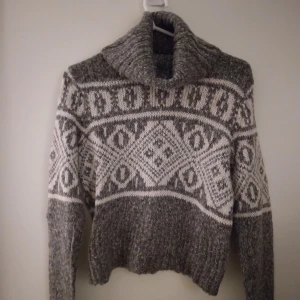 Grå och vit mönstrad stickad polotröja med mönster, XS, Felfri - Mysig något kortare polotröja i grått och vitt med mönster. Den har bred polokrage och är stickad i mjukt material. Perfekt för kalla dagar när man vill vara både chill och snygg. Långärmad och ribbad vid muddar och nederkant. Storlek XS-S. Felfri.