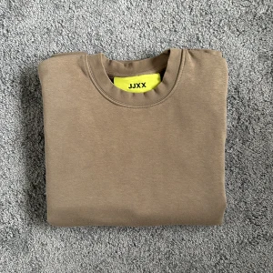 Beige sweatshirt från JJXX - En stilren beige sweatshirt från JJXX med rund halsringning och ribbade muddar. Tröjan är i mjuk bomull och har en relaxed passform som passar perfekt till jeans eller mjukisbyxor. Enkel och clean design utan tryck eller mönster.