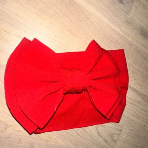 Rött diadem med stor rosett Rött hårband - Snyggt rött diadem med en riktigt stor och iögonfallande rosett framtill. Tillverkat i ett stretchigt tyg med struktur som ger en cool känsla. Perfekt accessoar för att lyfta din look och sticka ut i mängden.Rött hårband med en stor rosett. Perfekt för att addera en färgklick till din outfit. 🎁 🎅🏼 