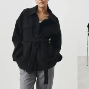 Svart kappa med bälte från Gina Tricot - Svart kappa från Gina Tricot i ullmix med knappar framtill och knytskärp i midjan. Jackan har klassisk krage, stora fickor och lång ärm. Perfekt för lager-på-lager och ger en chill men snygg vibe. Priset går att buda på🥰