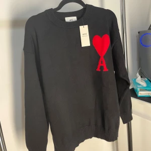 Ami Paris stickad tröja - Svart stickad tröja från Ami Alexandre Mattiussi med rund halsringning och stor röd hjärt- och A-logga på bröstet. Tröjan har ribbade muddar och är långärmad, perfekt för dig som gillar stilrena plagg med en twist.