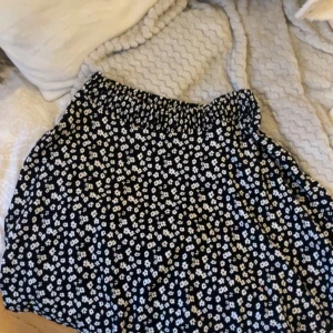 Svart blommig kortkjol med resår - Supersöt svart kortkjol med små vita blommor och bekväm resår i midjan. Perfekt för dig som gillar en avslappnad och trendig stil. Kjolen har en lätt och luftig känsla, vilket gör den enkel att matcha med olika toppar.