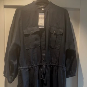 Marinblå klänning från Ralph Lauren - Snygg marinblå skjortklänning från Ralph Lauren med knappar framtill, två stora bröstfickor och snörning i midjan. Klänningen har en rak, avslappnad passform och är tillverkad i ett linne-material som känns luftigt och fräscht. Perfekt för dig som gillar stilren design med praktiska detaljer. Storlek: US 4 (EU 36), men modellen är ganska rymlig och passar därför även dig som brukar ha M. Helt ny, endast provad. Fler bilder kan skickas vid intresse! 