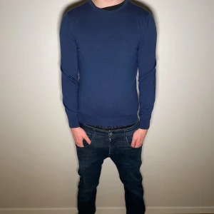 Blå stickad tröja från Stenströms - Snygg blå stickad tröja från Stenströms med rund halsringning och lång ärm. Tröjan har en klassisk passform och är tillverkad i mjukt material som känns skönt mot huden. Perfekt för lager-på-lager under kyligare dagar.Modellen är 183cm 69kg)