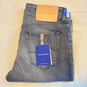 Helt nya Grå jeans Jacob Cohën Bard straight fit - Snygga grå jeans från Jacob Cohën, modell Bard. Jeansen har en klassisk femficksdesign, raka ben och diskret slitning framtill. Tillverkade i mjuk bomullsdenim med exklusiva detaljer och logotyp på bakfickan. Perfekta för en stilren och avslappnad look.
