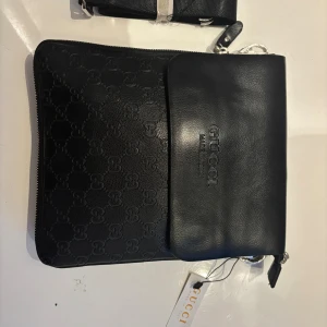 Helt ny Gucci väska  - Snygg svart axelväska från Gucci i äkta skinn med präglat GG-mönster på framsidan och diskret logotyp. Väskan har dragkedja upptill, extra fack med dragkedja på baksidan och justerbar axelrem. Perfekt storlek för det viktigaste och stilren design.