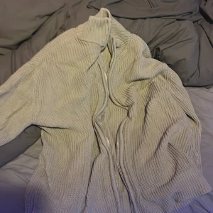 Beige ribbad kofta från 157 - Säljer en beige ribbstickad kofta från 157 med dragkedja framtill och hög krage. Koftan är långärmad och har en loose fit, perfekt för lager-på-lager under kyliga dagar.