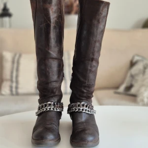 The Urban Project Stövlar * Brun * Stl 37/38 - Snygga bruna stövlar med kedjedetaljer.  * Märkt stl 37 men stor i storleken. Jag är en klassisk stl 38a och de är perfekta.  * Stövlarna har en kort dragkedja på insidan för att lätt få in foten. Också en kortare på baksidan om man vill ha dem lite vidare. * Supersköna. * Passar till det mesta. * Skafthöjd: 44 cm inkl klack. * Vidd där dragkedjan börjar: 18 cm * Stövelstöden ingår. * Tyvärr inte uppsmorda då mitt läderfett är slut.  Djur och rökfritt hem. Se bilder och förstora.