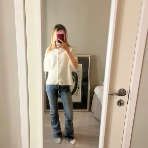 Vit stickad kofta från Gina Tricot - Säljer en vit stickad kofta från Gina Tricot i ullblandning. Koftan har korta ärmar, ribbad struktur och stora pärlemorknappar framtill. Använt ungefär 2 gånger.