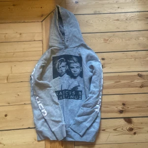 Grå hoodie från Marcus & Martinus - Säljer en grå hoodie från Marcus & Martinus med tryck av deras ansikten på framsidan och texten 'TOGETHER' på ärmen. Hoodien har en bekväm passform med långa ärmar och en klassisk huva. Perfekt för fans av duon!