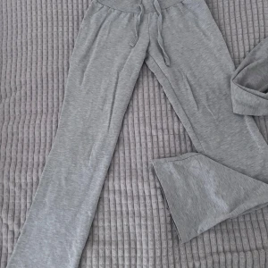 Grå ziptröja i mjukt material - Säljer en grå ziptröja i mjukt och stretchigt material. Tröjan har hög krage, hel dragkedja framtill och ribbade muddar vid ärmslut och nederkant. Perfekt för en chill och sportig look. Passar dig som gillar enkel och clean stil. Lågmidjade mjukisbyxor 