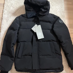Canada Goose - Säljer en svart Canada Goose black label Mcmillan. Aldrig använd då jag tyvärr köpte fel storlek till min sambo. Kan eventuellt gå ner i pris vid snabb affär!