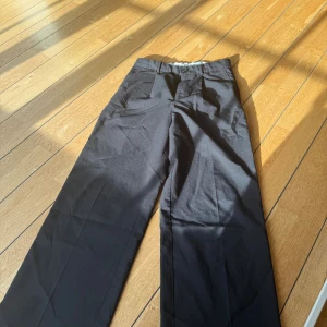 Svarta kostymbyxor med rak passform - Snygga svarta kostymbyxor med klassisk rak passform och pressveck. Byxorna har bälteshällor, knapp och dragkedja fram samt en bakficka med knapp. Perfekta för en clean och stilren look. Materialet känns som bomull eller polyester.