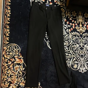 Svarta kostymbyxor Jack & Jones slim - Svarta kostymbyxor från Jack & Jones i slim fit-modell. Klassisk design med fickor fram och bak, bälteshällor och knappstängning. Perfekta för en clean och stilren look. Materialet känns mjukt och följsamt.