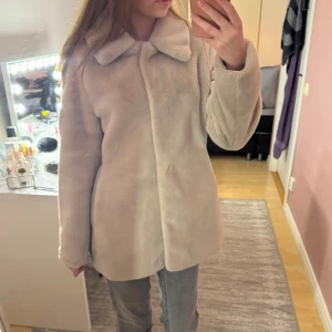 Beige pälsjacka med krage - Säljer en supermjuk beige pälsjacka med bred krage och knäppning framtill. Jackan har en clean look och är lite längre i modellen, perfekt för dig som vill ha en mysig och stilren vibe. Passar dig som gillar oversized känsla och vill hålla dig varm med stil.