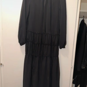 Svart långklänning med volanger - En svart långklänning med långa ärmar och flera volangdetaljer längs kjolen.