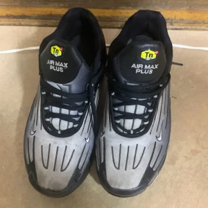 Nike Air Max Plus svart/grå sneakers - Nike Air Max Plus sneakers i svart och grått med coola svarta detaljer och Tn-logga på plösen. Skorna har snörning och en sportig vibe, perfekt för dig som gillar streetstyle. Ovandelen är i syntetmaterial och mesh för bra andningsförmåga.