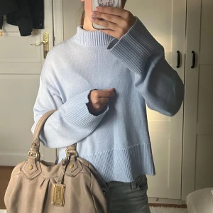 Ljusblå stickad tröja med hög krage - Superfin ljusblå stickad tröja med hög ribbad krage och breda muddar. Tröjan har en loose passform, slits i sidorna och är långärmad. Perfekt för lager-på-lager och chill vibes.