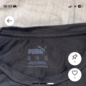 Svart Puma t-shirt med logga XS - Svart t-shirt från Puma i storlek XS med klassisk vit Puma-logga på bröstet. T-shirten har rund hals och korta ärmar, tillverkad i mjuk bomull som är skön mot huden. Perfekt för dig som gillar sportiga och stilrena plagg.
