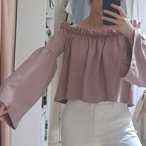 Ljuslila offshoulder blus NLY Trend - Supersöt ljuslila offshoulder blus från NLY Trend i storlek XS. Vida långa ärmar och rynkad resår upptill som ger en snygg volangkant. Croppad modell med flowig passform, perfekt till höga jeans eller kjol.