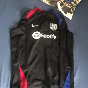Svart långärmad FC Barcelona Nike tröja - Säljer en svart långärmad FC Barcelona fotbollströja från Nike med Dri-Fit material. Tröjan har klubbmärke, Nike-logga och Spotify som sponsor på bröstet. Slim fit-modell med röda och blå detaljer vid axlar och sidor. Perfekt för dig som gillar Barca och vill ha något snyggt på träningen. Köpt från zalando 