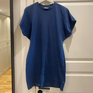 Mörkblå t-shirtklänning från Kappahl - Enkel och stilren mörkblå t-shirtklänning från Kappahl i mjuk bomull. Klänningen har rund halsringning, korta ärmar och rak passform. Perfekt för en avslappnad look och lätt att styla med sneakers eller sandaler.