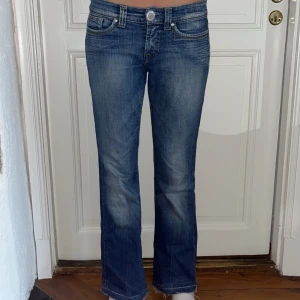 Blå bootcut jeans med låg midja - Snygga blå jeans med bootcut passform och låg midja. Jeansen har klassiska fem fickor, slitningar och ljusare partier framtill och baktill för en cool look. Tillverkade i jeansmaterial med detaljerade sömmar på bakfickorna. Pris går såklart att diskutera💕