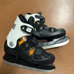 Svarta Rookie skridskor strl 35 - Säljer ett par svarta och vita skridskor från Rookie i storlek 35. De har coola orangea flames på sidorna, kraftiga spännen och kardborreband för extra bra passform. Yttermaterialet är syntet och insidan är mjukt textilfoder. Perfekta för isbanan! Pris kan diskuteras 