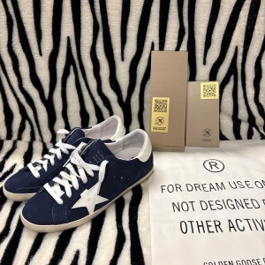 Golden Goose - Snygga sneakers från Golden Goose i mörkblå mocka med vit stjärndetalj på sidan och vit häl med logotyp. Skorna har vita snören, rund tå och platt sula i gummi. Perfekt för dig som gillar en cool och stilren look med exklusiv känsla. Og med följes Box, Dustbag & kort! 9/10 skick. Hör av dig vid funderingar 🫰🏻🤙