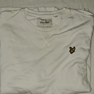 Vit sweatshirt från Lyle & Scott XL - Vit sweatshirt från Lyle & Scott i ekologisk bomull. Klassisk rund halsringning, ribbade muddar och det ikoniska gula örnloggan broderad på bröstet. Perfekt basic med clean look och skön passform.