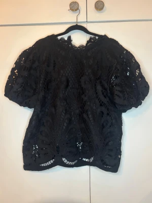 Svart spetsblus med puffärm - Svart blus i spets med korta puffärmar och vackra broderade detaljer. Blusen har en luftig och lite boxig passform, perfekt för utgång eller bara vara lite festligare! Använd fåtal gånger bara🫶🏻