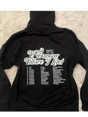 Svart Hov1 hoodie  - Svart hoodie från Hov1 storlek S med vit kronlogga framtill och stort turnétryck på ryggen med texten 'Vi Dansar Vidare I Livet' samt turnédatum. Klassisk passform med huva och dragsko.  Pris kan diskuteras 