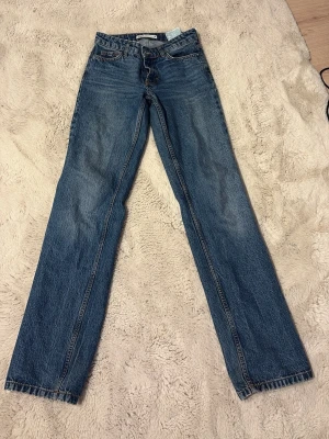 Blå raka jeans från Zara - Klassiska blå jeans från Zara med rak passform och normal midja. Jeansen har dragkedja och knapp framtill, samt fem fickor. Tillverkade i slitstarkt bomullsjeansmaterial med snygga kontrastsömmar. Inget är sönder! Dom har tyvärr blivit för små