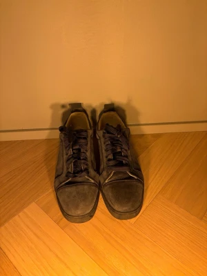 Mörkblåa Louboutin  - Snygga mörkblåa Louboutin med rund tå och platt sula. Skorna har snörning och en unik röd undersida med mönster. Materialet är mocka vilket ger en soft och stilren vibe. Perfekta för dig som vill sticka ut lite extra. De är i mycket bra skick. De är stora i storleken så de passar 40 också. Äkta!!