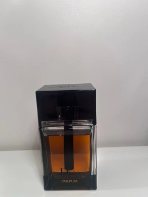 Dior Homme Parfum 75ml - Dior Homme Parfum i en elegant, fyrkantig glasflaska med svart lock och detaljer. Flaskan har en djup bärnstensfärgad vätska och en stilren design som utstrålar lyx och modernitet. Perfekt för dig som gillar exklusiva dofter. Endast använd få gånger!
