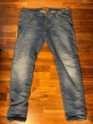 Blå slim fit jeans från Jack & Jones - Snygga blå slim fit jeans från Jack & Jones med klassisk femficksdesign och slitna detaljer. Jeansen har normal midja, dragkedjegylf och är tillverkade i mjuk denim med lite stretch för extra komfort. Perfekta för en avslappnad och trendig look.
