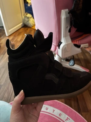 Svarta höga sneakers med kardborre - Liknar Beckett skorna. Svarta sneakers med högt skaft och cool design. Skorna har flera kardborreband istället för klassisk snörning och en brun sula. Materialet är en mix av mocka och syntet. Perfekta för dig som vill sticka ut med en unik look. Storlek 40 men har själv 39 och passar mig, endast använda en gång!