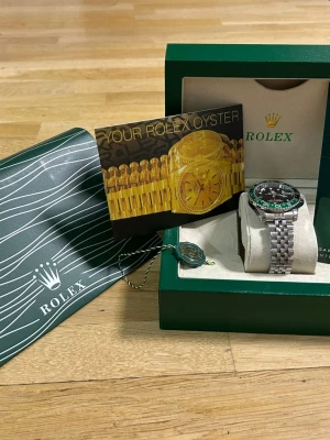 GMT-Master II klocka stål/grön - Säljer en GMT-Master II med svart urtavla och grön/svart vridring. Klockan har en robust länk i rostfritt stål och klassisk design. Kommer med originalbox, certifikat och tillbehör. Perfekt för dig som gillar exklusiva accessoarer och tidlös stil.