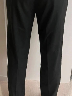 Svarta kostymbyxor från MNG - Stilrena svarta kostymbyxor från MNG med klassisk rak passform och resår i midjan. Byxorna har bälteshällor och sidofickor, perfekta för en clean och modern look. Materialet känns mjukt och följsamt.