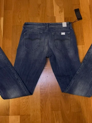 Blå raka jeans med detaljerad bakficka - Snygga blå jeans från Replay med raka ben och coola detaljer på bakfickorna. Jeansen har klassisk femficksdesign, normal passform och är tillverkade i mjukt denimtyg. Perfekta för en avslappnad och trendig look. Storlek W27 L34