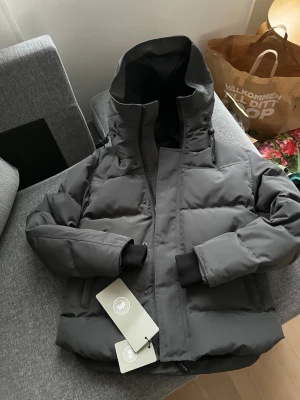 Mörkgrå Candada Goose jacka - Snygg mörkgrå jacka från Canada Goose.  Jackan har en quiltad design och dragkedja framtill. Perfekt för kalla vinterdagar och riktigt stilren look. Passar inte mig pågrund av fel storlek
