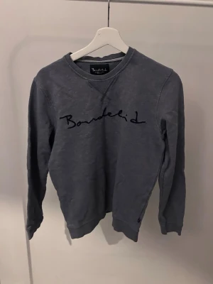 Grå sweatshirt från Bondelid - Mysig grå sweatshirt från Bondelid med broderad logga framtill. Tröjan har rund halsringning, långa ärmar och ribbade muddar vid ärmslut och nederkant. Perfekt för en avslappnad och stilren look.